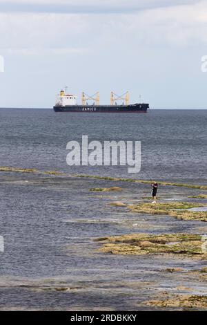 Lone man sea fishing out at sea with large ship in background near Whitley Bay Stock Photo