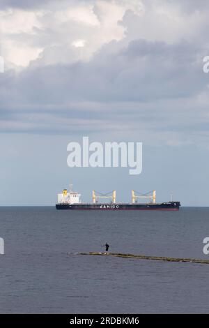 Lone man sea fishing out at sea with large ship in background near Whitley Bay Stock Photo