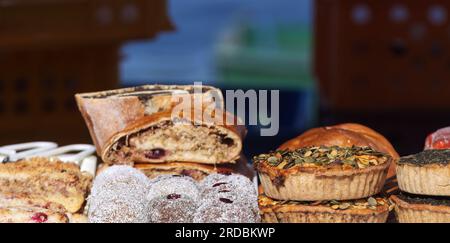 Stand with fresh sweet and savoury pastries on display at the Naplavka Farmers Market, closeup of salty quiche sprinkled with pumpkin seeds, sweet bal Stock Photo