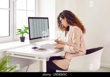 Focused businesswoman analyzing financial spreadsheet report on computer screen Stock Photo