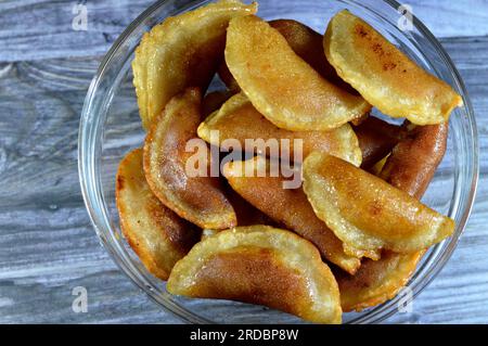 A bowl of qatayef dumplings stuffed and filled with nuts and shredded coconut fried in deep oil and soaked with sugar syrup, Arabic dessert folded pan Stock Photo