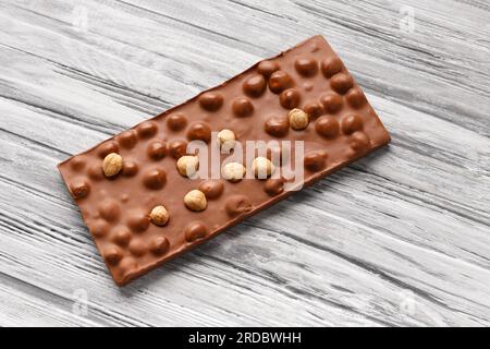 Handmade chocolate with whole hazelnuts on a gray wooden background, top view, space for text, milk chocolate bar with nuts, concept for patisserie. Stock Photo