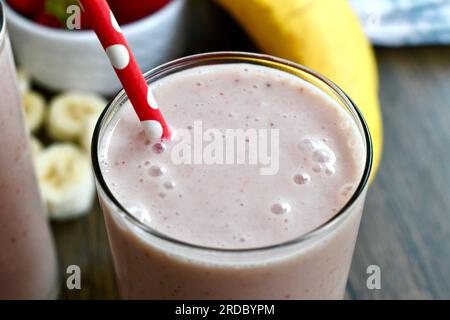 Strawberry banana smoothie in a clear glass on a rustic surface Stock Photo