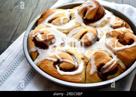 Cinnamon rolls in a round baking pan on a rustic wooden table Stock Photo