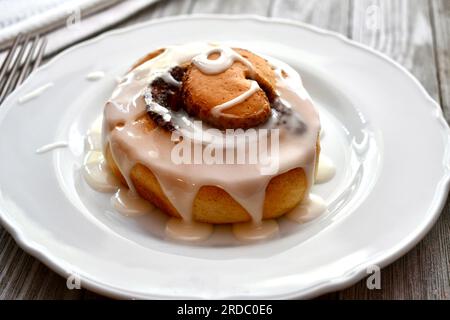 Cinnamon roll drizzled with icing on a white plate Stock Photo