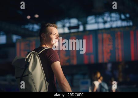 Traveling by airplane. Portrait of man walking through airport terminal against flight information board. Stock Photo