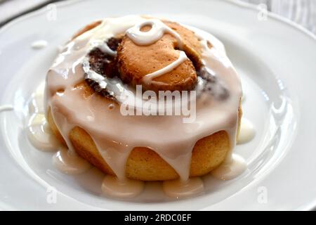 Cinnamon roll drizzled with icing on a white plate Stock Photo