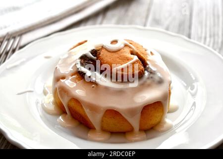 Cinnamon roll drizzled with icing on a white plate Stock Photo
