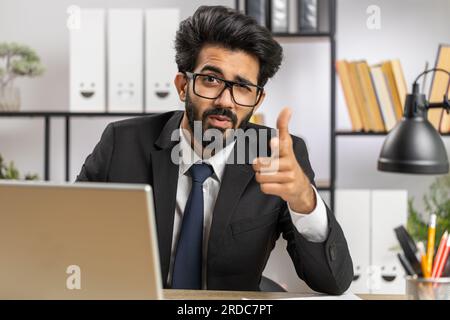 I choose you. Young indian businessman programmer software developer working on office laptop pointing to camera, looking with happy expression, making choice, showing direction. Arab freelancer man Stock Photo