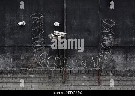 CCTV security cameras and barbed wire on the exterior of a factory building, UK Stock Photo