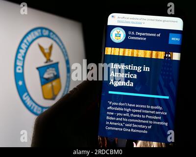 Person holding cellphone with webpage of the United States Department of Commerce (DOC) on screen with seal. Focus on center of phone display. Stock Photo