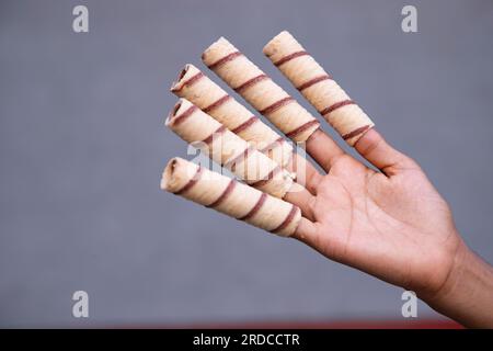 Hand-holding wafer rolls with chocolate on gray background, close up Stock Photo