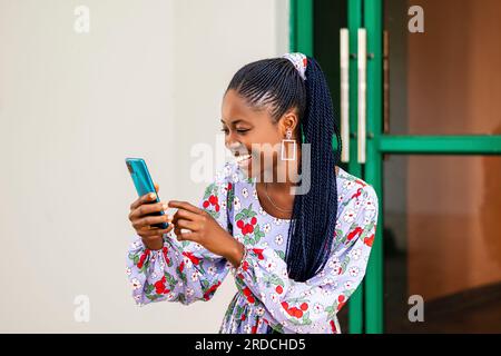young joyful African woman smiling while using her cell phone Stock Photo