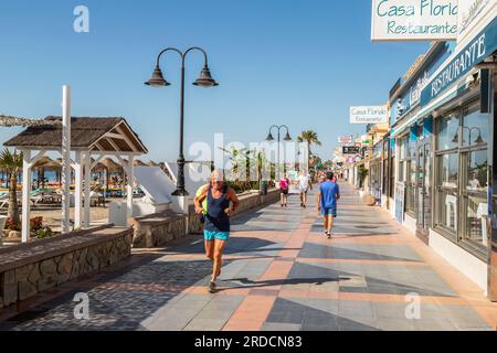 Older vital man running on the boulevard of the popular Mediterranean resort of La Carihuela with its summer beach life. Stock Photo