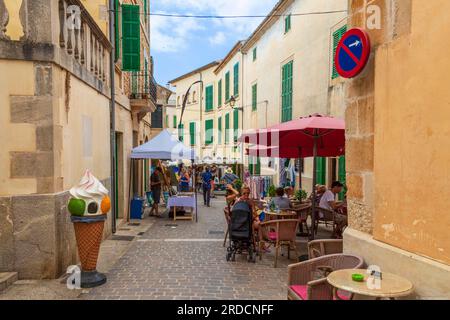 People stroll down a cozy narrow street lined with merchandise stalls in the picturesque town of Santanyí on the Mediterranean island of Majorca in Sp Stock Photo