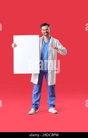 Male dentist with brush and big plastic tooth on red background Stock Photo