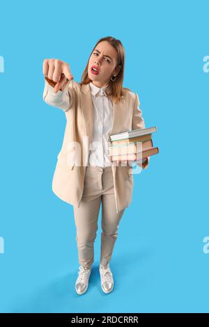 Upset young woman with books pointing at viewer on blue background Stock Photo