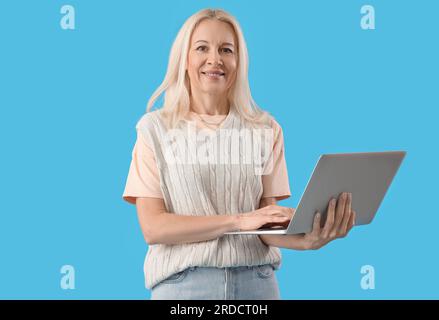 Mature female programmer working with laptop on blue background Stock Photo