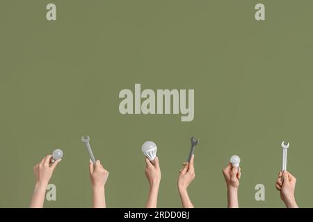 Electrician hands with light bulbs and wrenches on green background Stock Photo