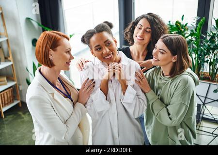 positive psychologist and multiracial female friends hugging pleased african american woman during psychological coaching, moral support and mental we Stock Photo