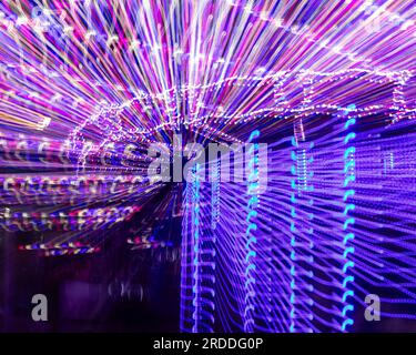 Amusement Ride at night, long exposure in camera movement, abstract pattern of pink, purple, and blue light streaks on a dark background Stock Photo