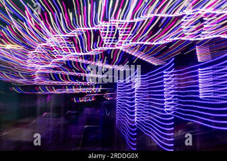 Amusement Ride at night, long exposure in camera movement, abstract pattern of pink, purple, and blue light streaks on a dark background Stock Photo