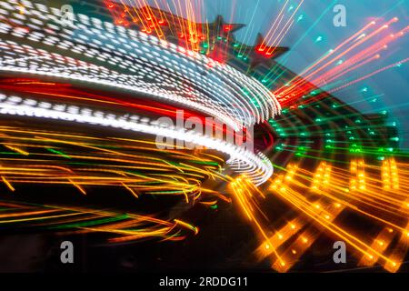 Amusement Rides, long exposure in-camera movement, abstract red, yellow, orange, and green light streaks against a blue background. Stock Photo