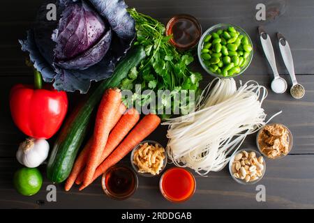 Rice Noodle Salad with Spicy Peanut Sauce Ingredients: Uncooked rice noodles and fresh vegetables and spices on a wooden table Stock Photo