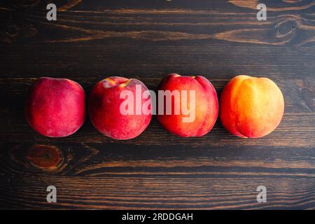 Row of Four Peaches on a Wooden Background: Fresh peaches grouped on a dark wood background Stock Photo