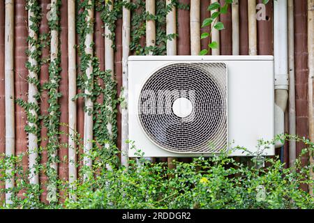 The air conditioner is mounted on the wall with the trees of the building with the garden in the front row. Stock Photo