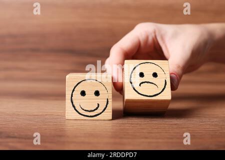 Complaint. Woman choosing cube with drawn sad face instead of another one with happy on wooden table, closeup Stock Photo