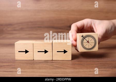 Woman putting cube with icon of target into row of cubes with arrows against on wooden background, closeup Stock Photo