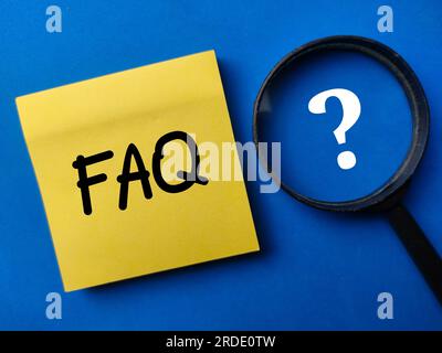 Magnifying glass and sticker note with the word FAQ on a blue background Stock Photo