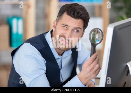 man looking at computer through a magnifying glass Stock Photo