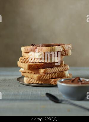 heap of toasted bread slices with chocolate cream on wooden kitchen table Stock Photo