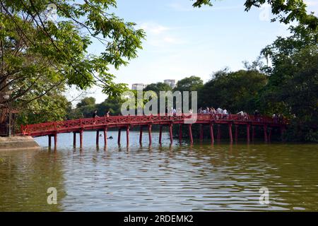 Tourists walk across Red Bridge leading to Ngoc Son Temple, a bridge over Hoàn Kiếm Lake, also known as Sword Lake or Tả Vọng Lake, is a fresh water lake, in central Hanoi, the capital city of Vietnam ,Asia; in past, the lake had been titled: 'Lục Thủy Lake' or 'Thủy Quân Lake' Stock Photo