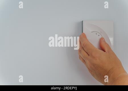Woman adjusting the dial on thermostat, lowering the temperature to save money on energy bills during the cost of living crisis Stock Photo