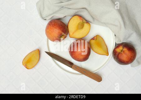 Cut peaches with knife on plate (Prunus persica) Stock Photo