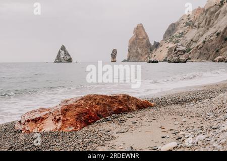 Large red jasper rock on the beach, with the sea in the background. Big Red Jasper Stone Close Up Stock Photo