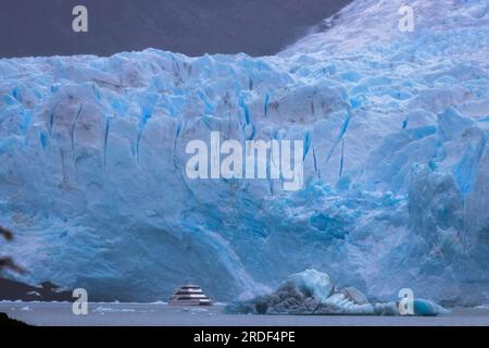 cracks and blues in the front of a glacier with a ship in foreground Stock Photo