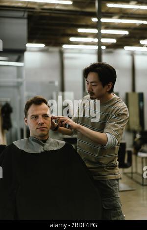 A Japanese barber cuts the hair of a man client at a barbershop. Stock Photo
