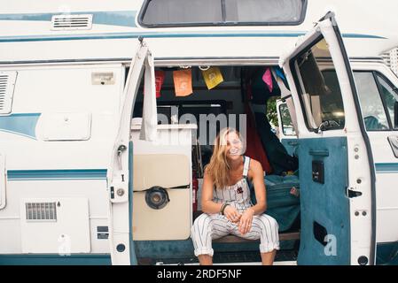Young Woman Smiling Sitting in Teal Camper Van Stock Photo