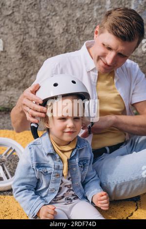 Father putting on a safety helmet for daughter to ride balance bike Stock Photo