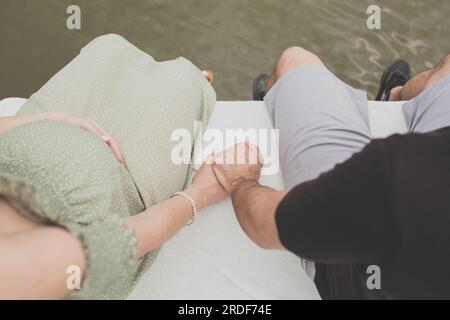 Expecting Couple Holding Hands while Sitting on Dock Stock Photo