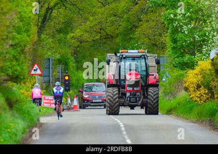 BEAULY, SCOTLAND, UK - 17 May 2022 - Two cyclists wait at a contraflow traffic light as a tractor and other vehicles pass through near Beauly, Inverne Stock Photo