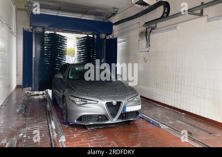 Front view of motor vehicle sporty sedan Italian make automobile Alfa Romeo Giulia being sprayed in car wash with car shampoo chemical care Stock Photo