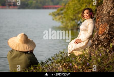 A middle aged Vietnamese woman wearing a traditional 'Ao Dai' poses for a photograph next to Hoan Kiem Lake in central Hanoi, Vietnam. Stock Photo