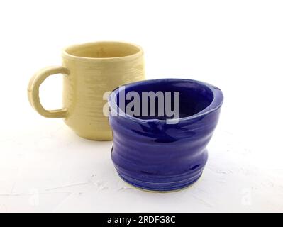 Color ceramic dishes on a white background. Cup made of blue clay covered with glaze and beige cup with handle. Empty cups in stack. ceramic products Stock Photo