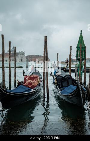 Venice,  Italy - April 27, 2019 : A wooden pier with a lantern, gondolas, and a gondolier passing in the background in Venice Italy Stock Photo