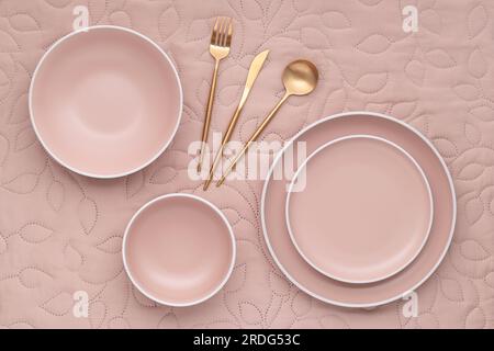A set of cream color plates of different sizes on table, top view. Gold cutlery and serving utensils. Empty dishes on light beige fabric tablecloth. M Stock Photo